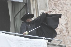 Il manifestante vestito da Zorro srotola uno striscione da un balcone in piazza DUomo: "Restiamo umani"