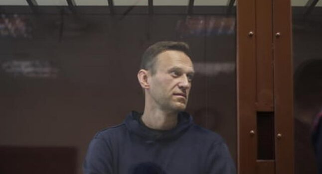 Aleksei Navalny in carcere costretto a lavorare alla macchina da cucire sotto un ritratto di Putin