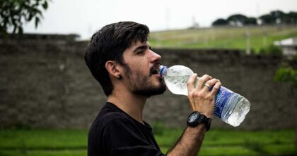 giovane adulto beve da una bottiglia di plastica
