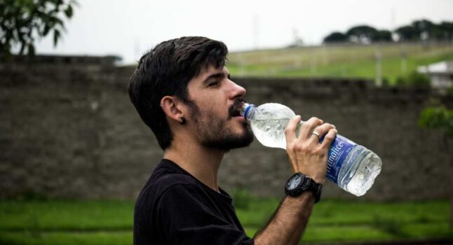 giovane adulto beve da una bottiglia di plastica